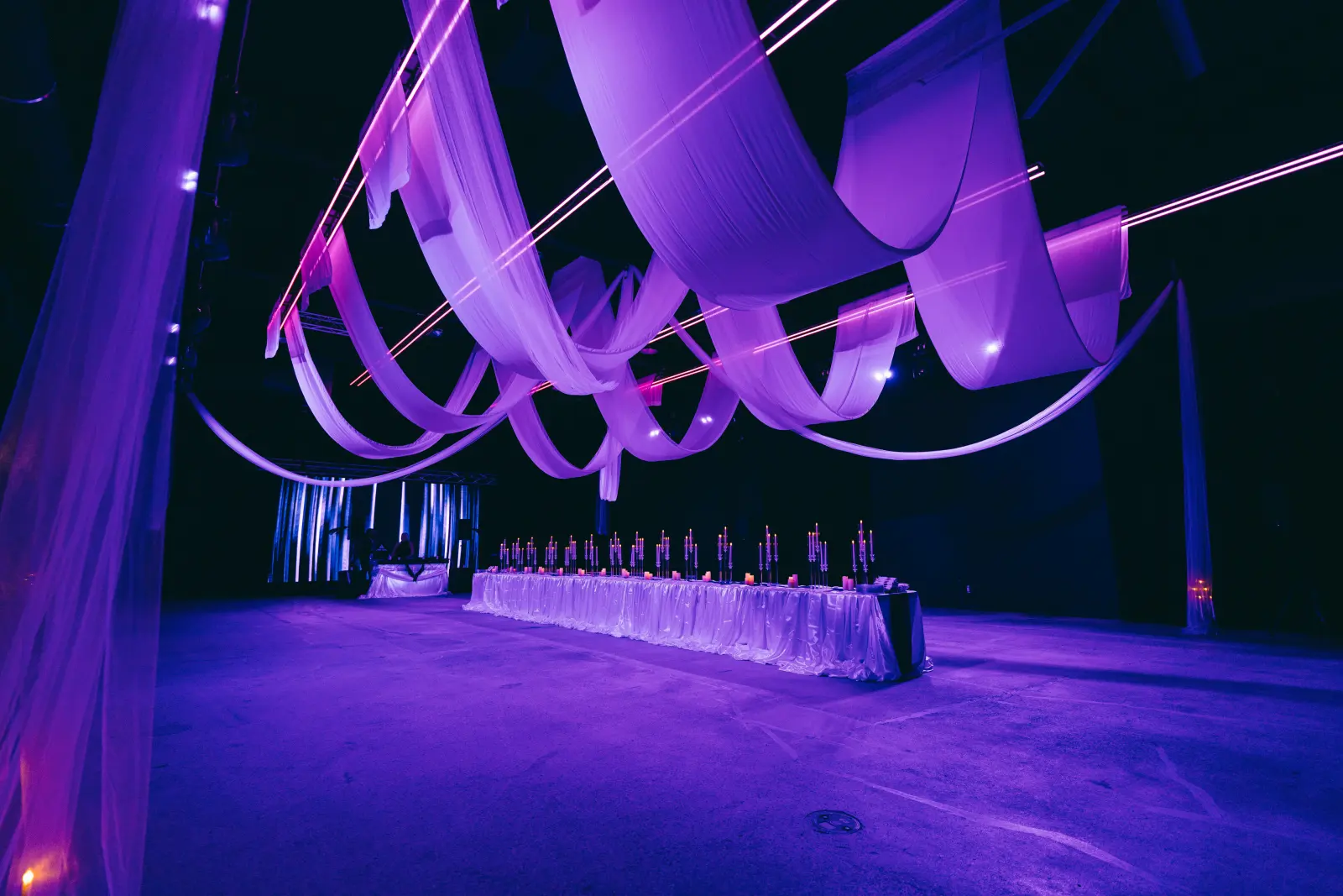 Long candlelit dinner table beneath a draped fabric ceiling installation at Demo Room