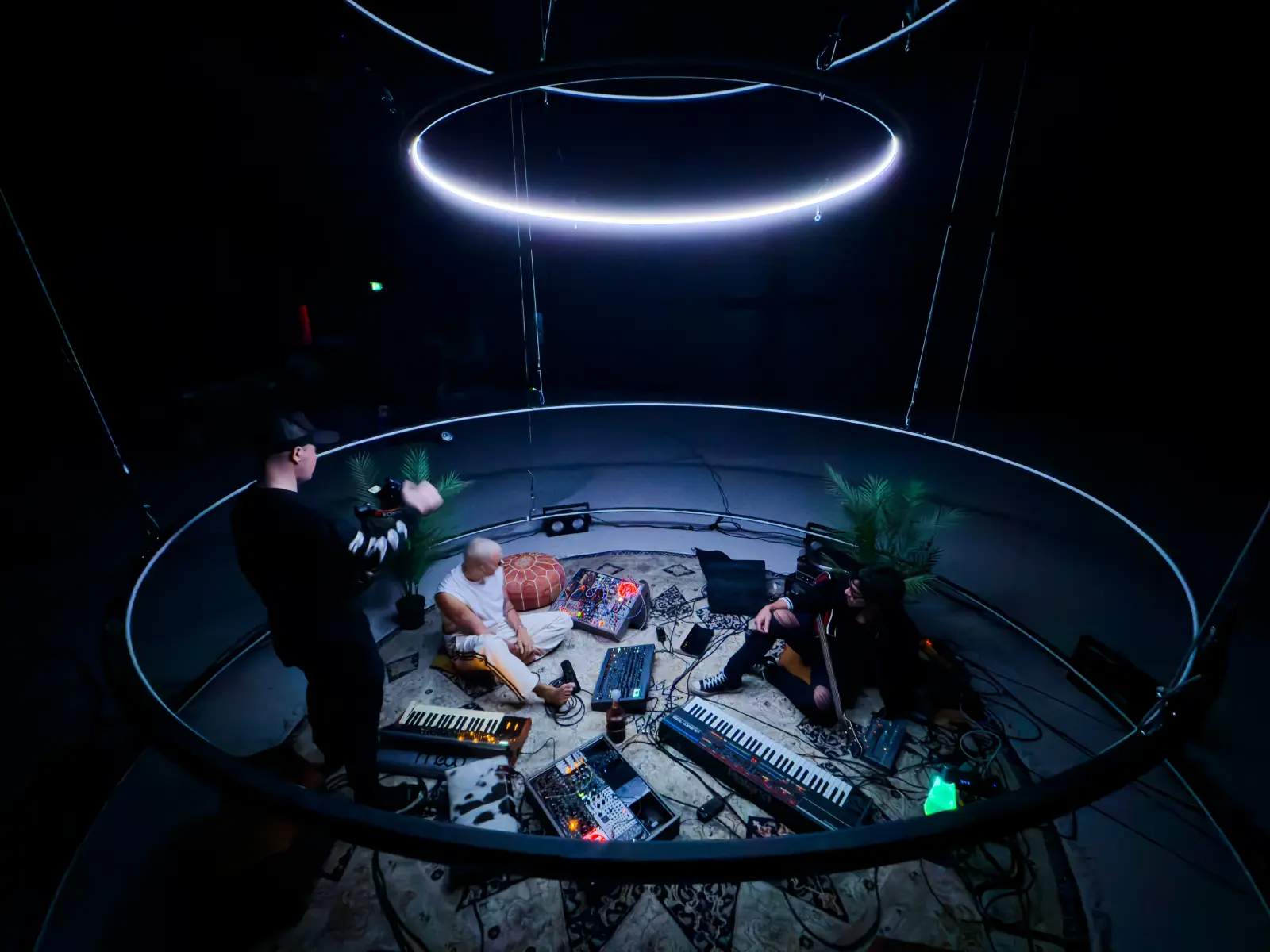 Camera crew filming musicians on the circular production floor beneath suspended lighting rings