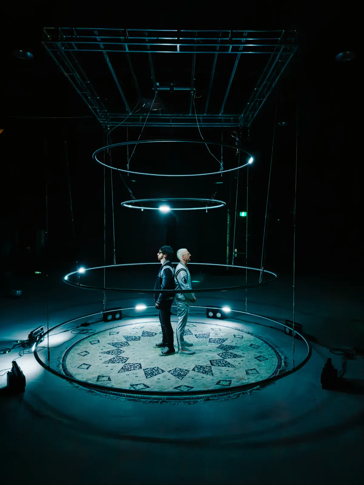 Two performers standing beneath the glowing suspended lighting rings, video still