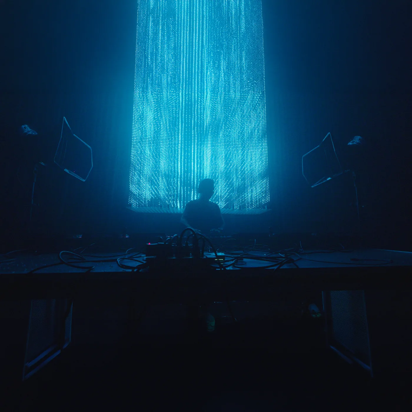 DJ performing at Demo Room beneath a suspended LED light curtain