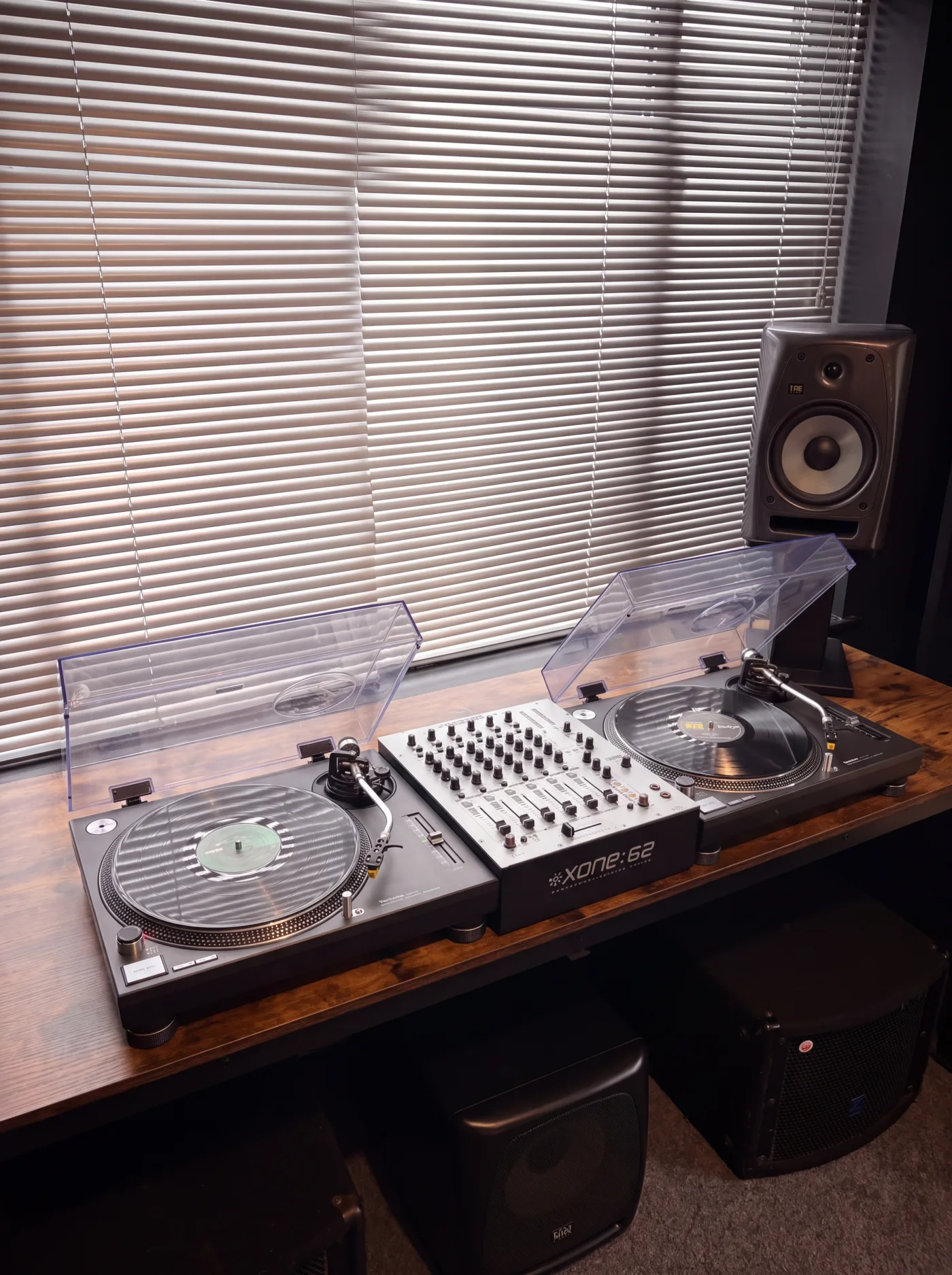 Demo Room vinyl room: two turntables and a DJ mixer on a wood desk beneath a studio monitor
